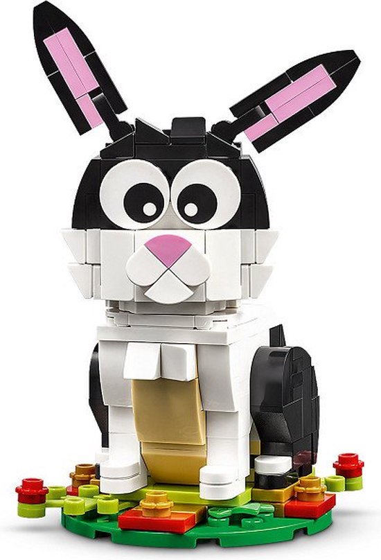 Un lapin LEGO en briques noires, blanches et beiges, avec de grands yeux et l'intérieur rose des oreilles, assis sur une base verte avec des fleurs.
