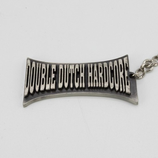 Zilverkleurige sleutelhanger met reliëftekst 'DOUBLE DUTCH HARDCORE' op een gebogen zilveren plaat.