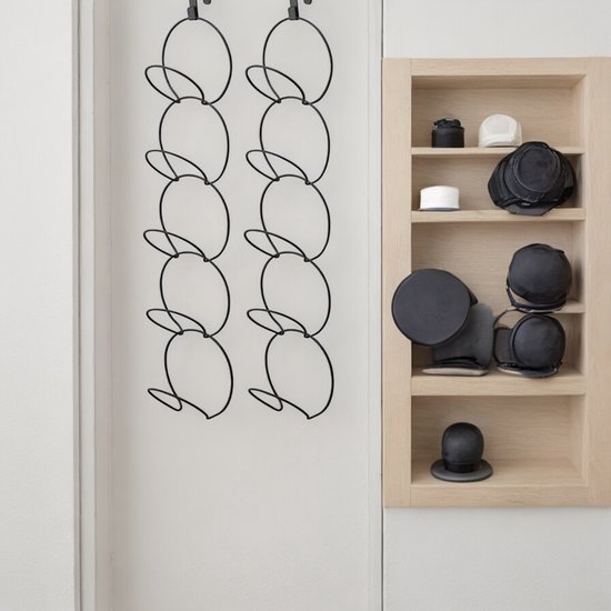 Zwarte hoedenhouders aan een muur en een houten kast met zwarte hoeden en witte mutsen.