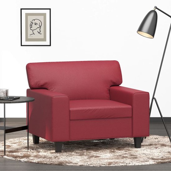 Moderne wijnrode kunstleren fauteuil op donkere pootjes, in een woonkamer setting.
