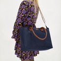 Model met bloemenjurk, draagt een donkerblauwe nylon tas met bruine handvatten en een afneembare band.