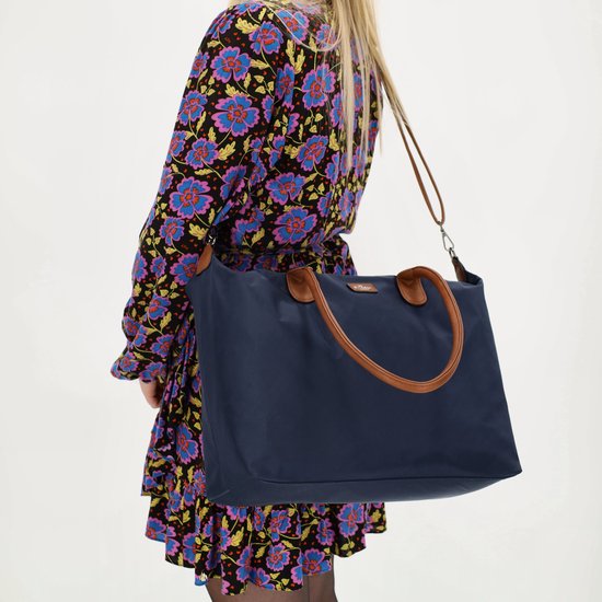 Model met bloemenjurk, draagt een donkerblauwe nylon tas met bruine handvatten en een afneembare band.