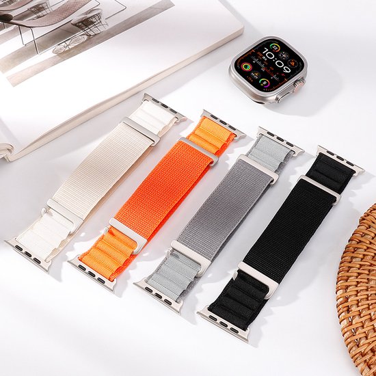 Vier Alpine Loop bandjes in crème, oranje, grijs en zwart, naast een smartwatch.