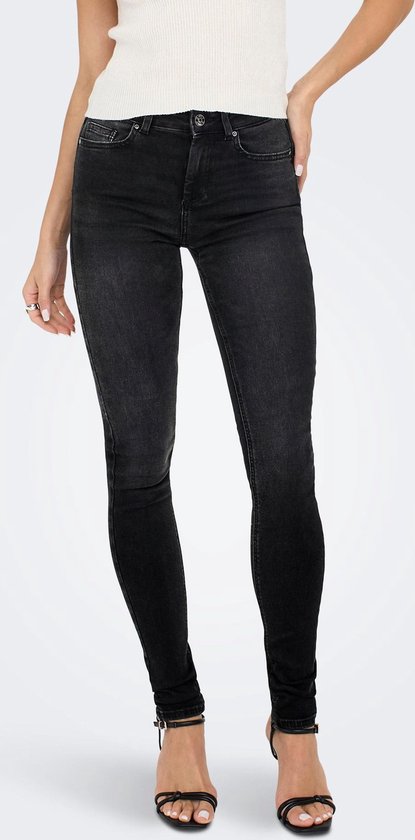 Model in strakke zwarte jeans met hoge taille, witte top en zwarte sandalen.