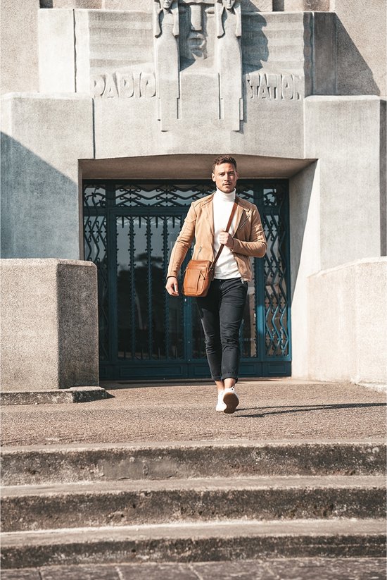 Man met bruine leren schoudertas, wit shirt en beige jas, lopend op een stenen trap.