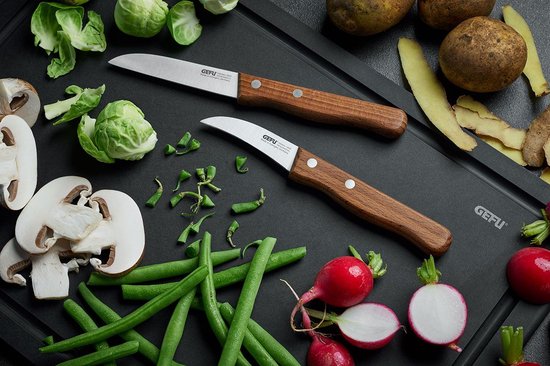 Twee GEFU groentemessen met houten handvatten liggen op een zwarte snijplank tussen groenten.