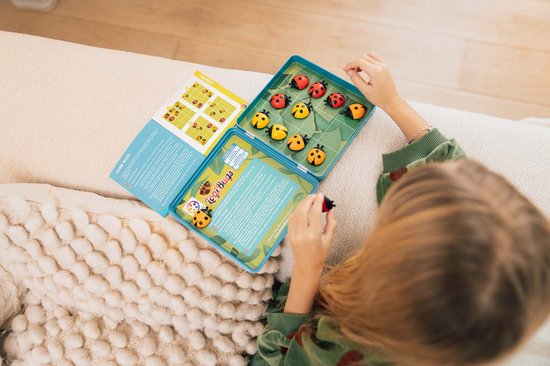 Une fille joue à LogiBugs, avec le plateau de jeu ouvert rempli de coccinelles.