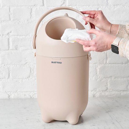 Een beige Nattou luieremmer met een persoon die een luier in de opening deponeert.