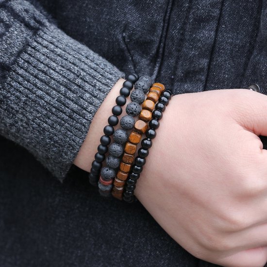 Set van vier armbanden met zwarte kralen, lavasteen en houten kralen om de pols van een man gedragen.
