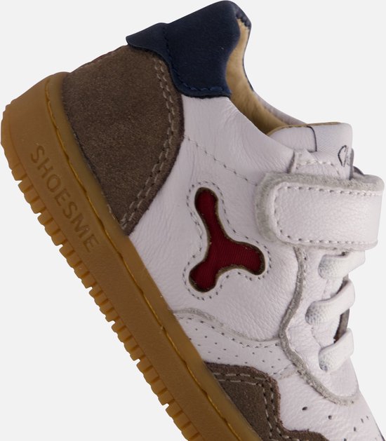 Close-up van de hiel en zijkant van een witte leren babyschoen met bruine suède en donkerblauwe lip.