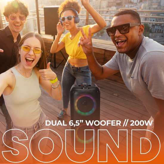 Twee luidsprekers met dubbele woofers met regenboogkleurige LED-verlichting, naast lachende mensen op een dakterras.