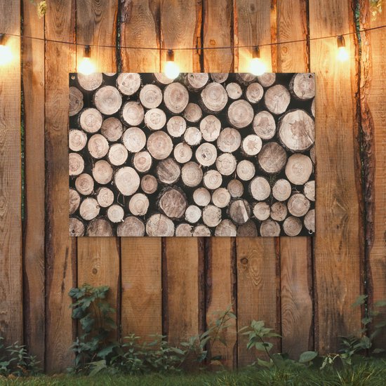 Une affiche avec des bûches empilées de différents diamètres et teintes naturelles, accrochée à une clôture en bois, décorée de lumières.