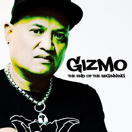 DJ Gizmo met een dikke zilveren ketting om, die een zwarte t-shirt draagt met een grafische opdruk. De tekst 'Gizmo THE END OF THE BEGINNING' staat ernaast.