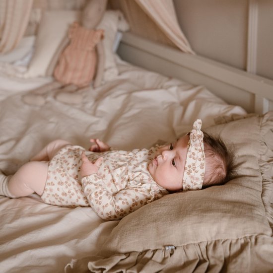 Baby ligt op bed met een beige romper met bloemenprint en bijpassende hoofdband.