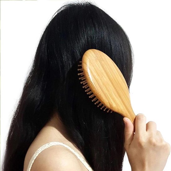 Vrouw met lang, donker haar borstelt haar haar met een ovale bamboe haarborstel.