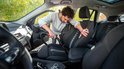Man stofzuigt autostoel met rode slang en grijze stofzuiger.
