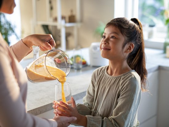 Kind kijkt toe hoe smoothie uit kan wordt geschonken.