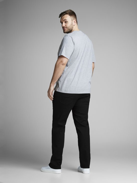 Man in een grijze T-shirt en zwarte jeans, staat met de rug naar de camera.