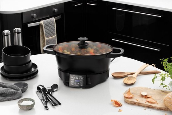 Zwarte Russell Hobbs multicooker met deksel op een witte tafel, met stoofpot erin.