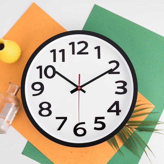 Witte wandklok met zwarte cijfers en wijzers op een oranje en groene achtergrond.