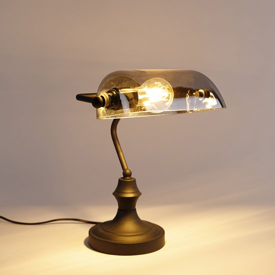 Lampe de banquier noire avec abat-jour en verre gris et ampoule visible, lumière tamisée.