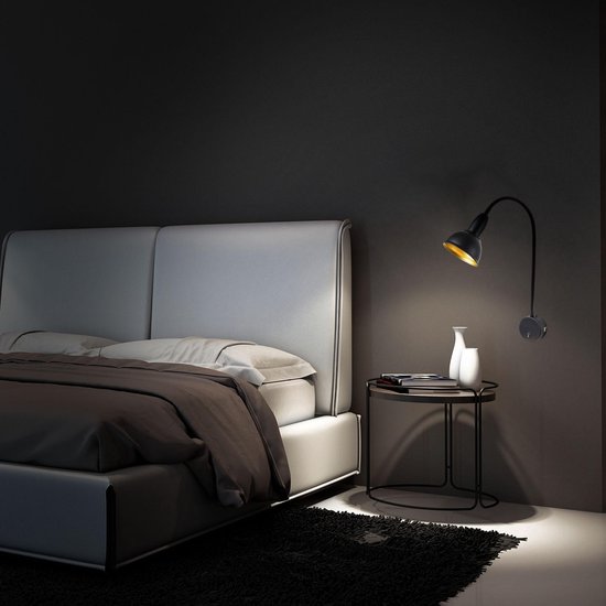 Zwarte, flexibele wandlamp met goudkleurige kap verlicht een bed in een slaapkamer.