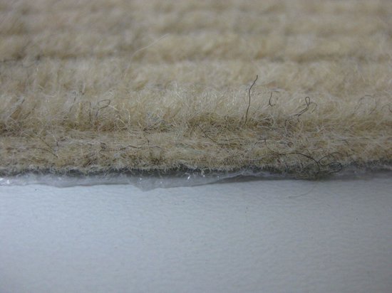 Zij-aanzicht van de beige stof van een trapmat met zachte vezels en antislip onderkant.