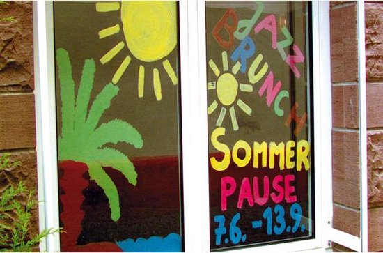 Fenêtre peinte avec des dessins ensoleillés et texte "Jazz Brunch Sommer Pause 7.6 - 13.9."