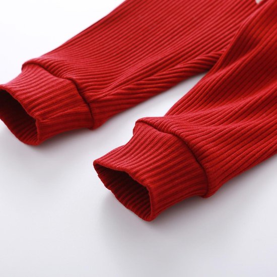 De geribbelde broekspijpen van de rode broek met elastische boorden.