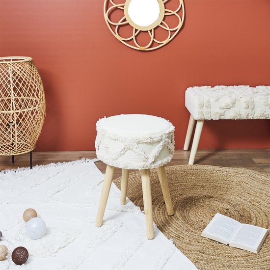 Beige krukje met ronde zitting en decoratieve franjes, op houten poten. Staat op een rond vloerkleed.