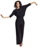 Model in een zwarte, wijde driekwartmouw top en zwarte broek met hoge taille, armen gespreid in een danshouding.