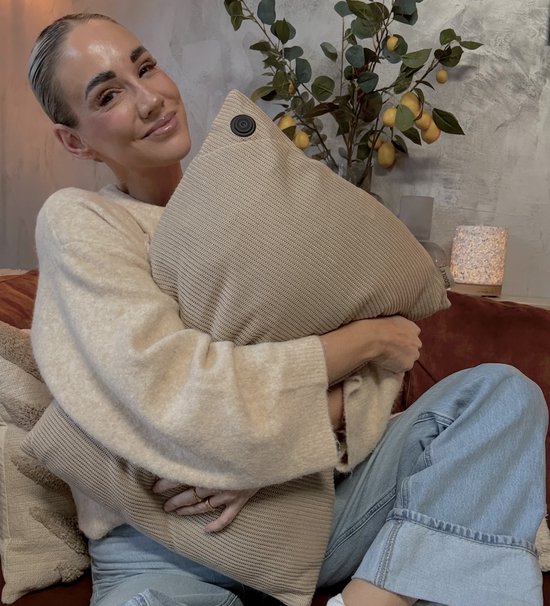 Vrouw omhelst zandkleurig gebreid kussen met geribd patroon en donkere knoop.