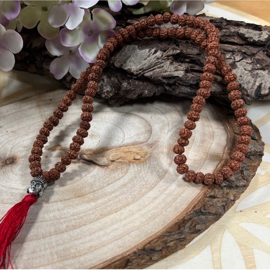 Collier mala Rudraksha marron avec tête de Bouddha argentée et gland rouge, posé sur du bois.