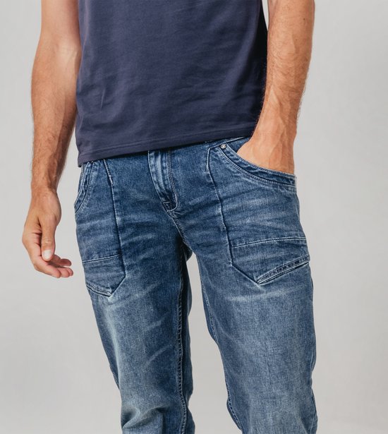 Blauwe spijkerbroek met stonewash-effect. Een man met zijn hand in de zakken van de broek.