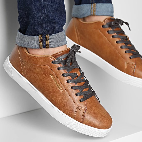 Voeten in bruine Jack & Jones sneakers met witte zolen en donkergrijze veters, gecombineerd met spijkerbroek.