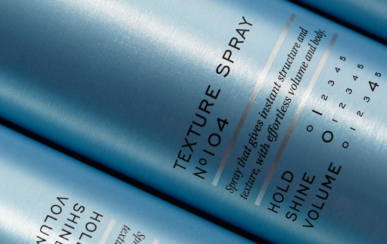 Close-up van blauwe REF textuursprayflessen, met tekst over hold, shine en volume.