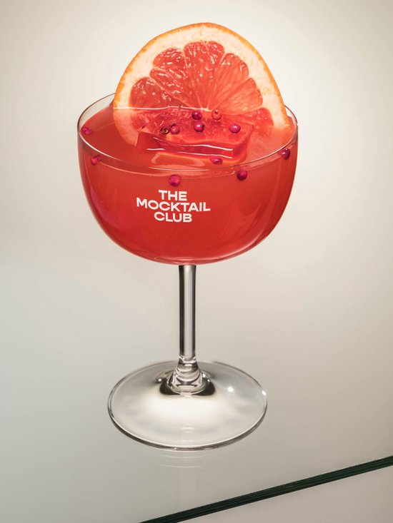 Glas met grapefruit mocktail, gegarneerd met een schijfje grapefruit, ijs en roze peperkorrels.