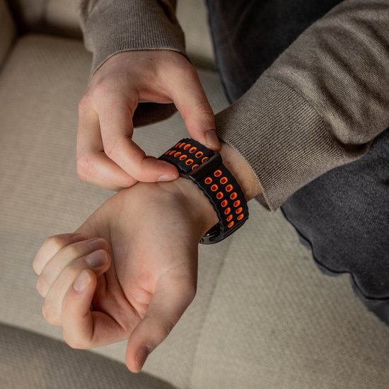 Man's pols met zwart en oranje siliconen horlogebandje.