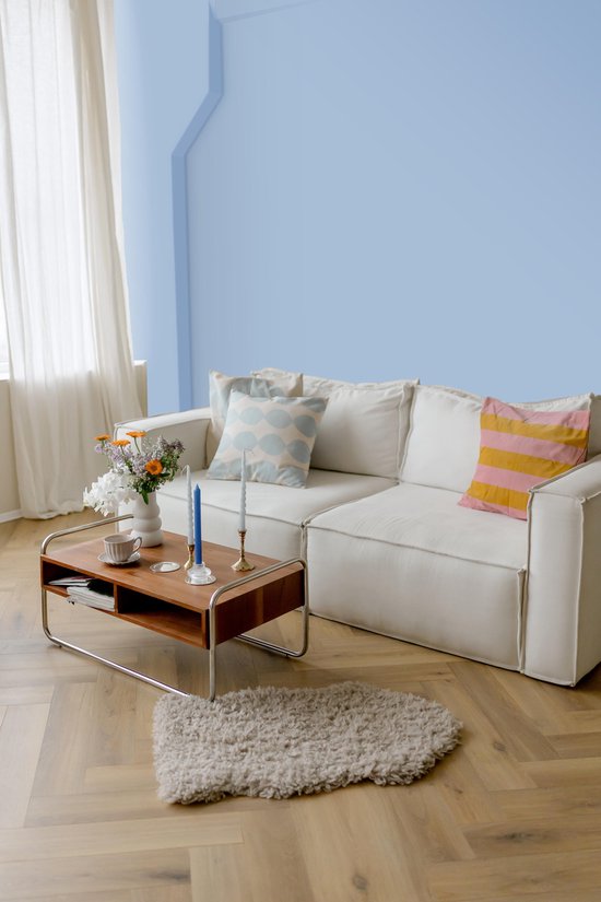 Lichtblauwe muurverf in een woonkamer met een witte bank en een houten salontafel.