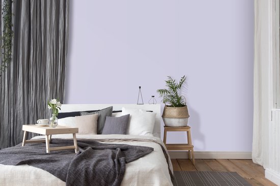 Slaapkamer met bed in zachtlila tinten, gedrapeerde grijze gordijnen en een nachtkastje met plant.
