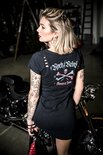 Vrouw met getatoeëerde armen in zwarte jurk met gescheurde schouders, 'Rock/Rebel' en doodshoofdprint.