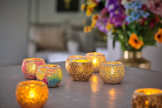 Meerdere mozaïek waxinelichthouders met LED kaarsjes erop, met een vaas met bloemen op de achtergrond.