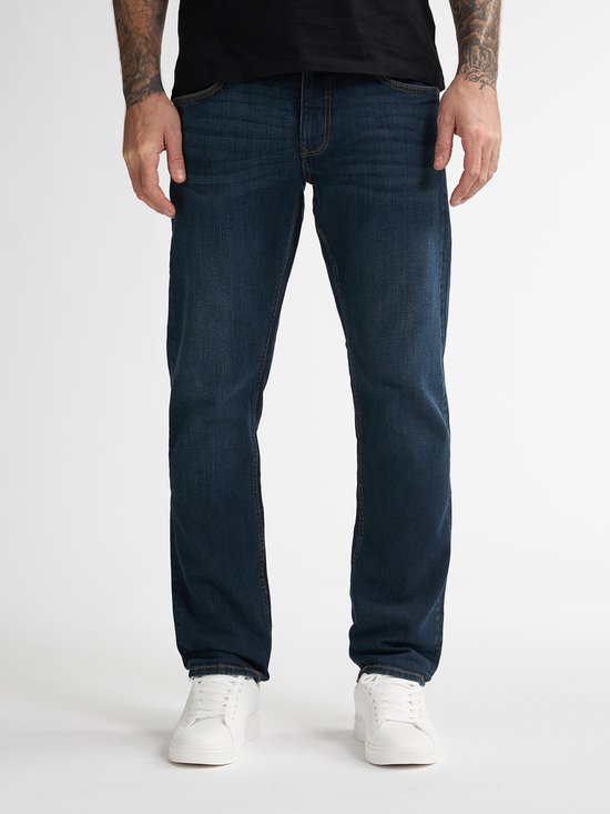 Detail van een donkerblauwe jeans, gedragen met witte sneakers.