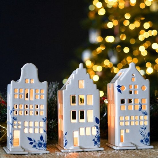 Drie witte keramische huisjes met blauwe bloemenmotieven, verlicht met waxinelichtjes, voor een kerstboom.