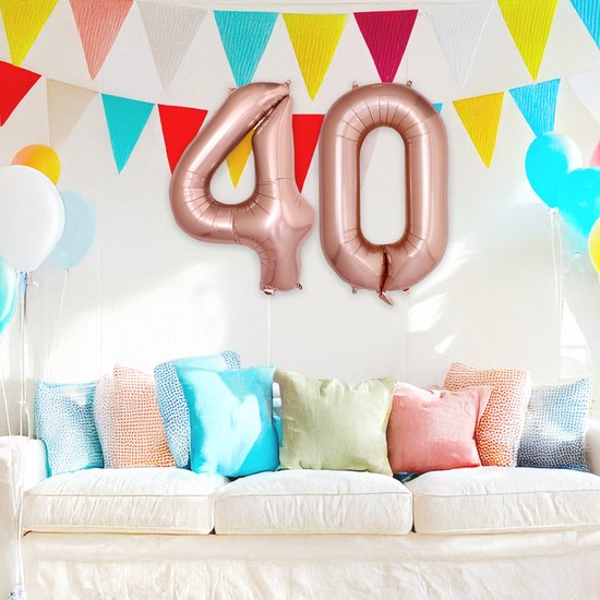 Kamer decoratie met ballonnen: rosegouden cijfer 40 ballonnen, witte en blauwe ballonnen, gekleurde slingers en kussens op een bank.