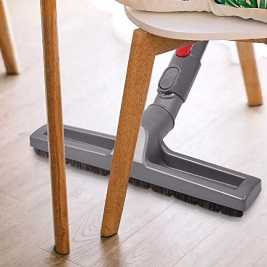 Grijze parketborstel met borstels onder de grijze behuizing, onder een witte stoel.