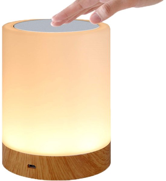 Cilindrisch lampje met houten basis, verlicht met een warme, gele gloed. Een hand raakt de bovenkant aan.