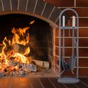 Grijze haardset met schep, pook, tang en bezem op een ronde houder, naast een brandende open haard.