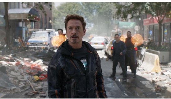 Iron Man in een donker jack staat op een straat vol brokstukken.