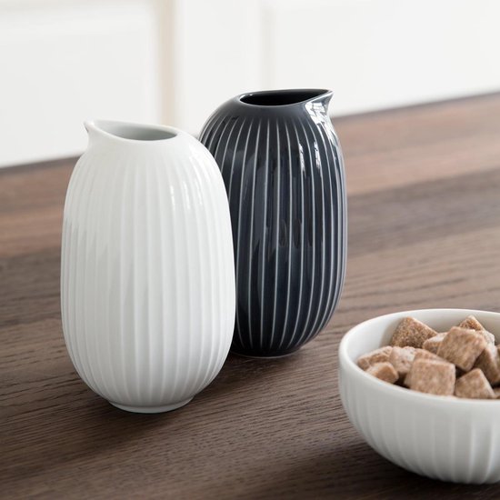 Witte en donkergrijze karaf met verticale ribbels op een houten tafel naast een kom met suikerklontjes.